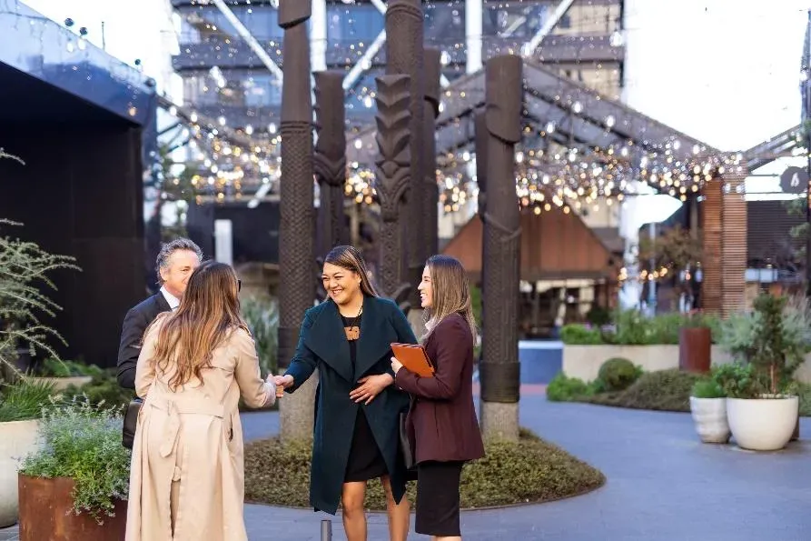 People shaking hands in from of some carved Māori poles